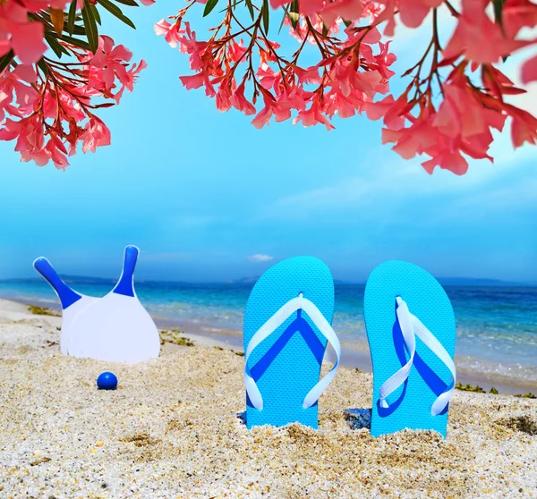 Sandals and beach rackets under pink flowers — Stock Photo, Image