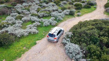 Toprak bir yolda sörf tahtası taşıyan bir cipin yukarıdan görünüşü. Parlak manzara ve açık çevre, Sardunya İtalya 'da sinematik bir kıyı ya da çöl atmosferi yaratır..