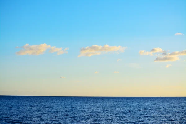 Mar azul sob um céu claro com pequenas nuvens — Fotografia de Stock