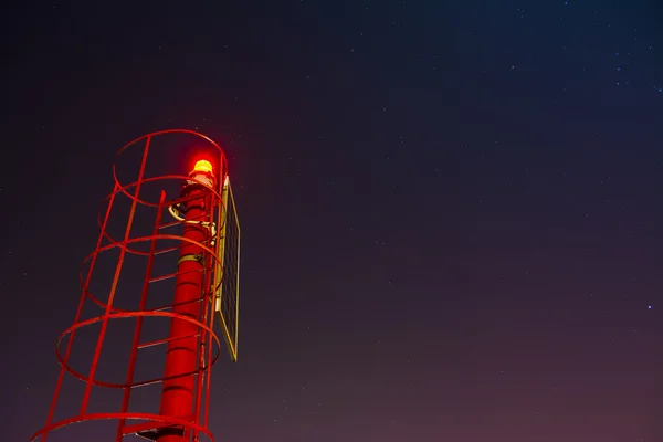 Pequeno farol vermelho sob um céu estrelado — Fotografia de Stock