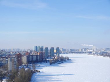 Nehrin kıyısındaki gökdelenler kardan bembeyaz, ufukta büyük bir şehir manzarası 