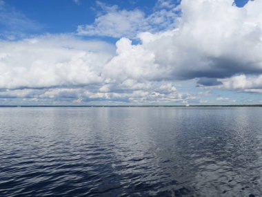 Deniz manzaralı kümülüs bulutları ve mavi gökyüzü denize yansıyor.