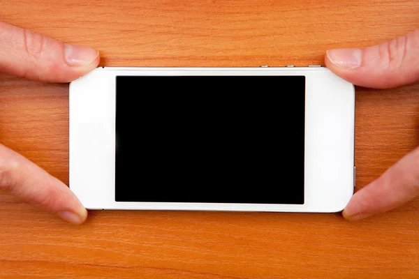 Chica sosteniendo teléfono inteligente blanco en una mesa de madera —  Fotos de Stock