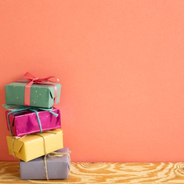 Ahşap masada mercan pembesi arkaplanlı renkli hediye kutuları yığını.