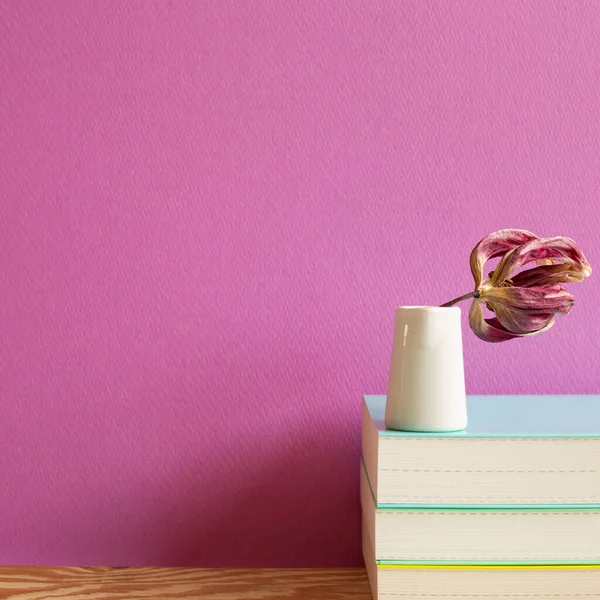 Books with dry flower on wooden desk. pink background