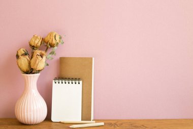 Boş bir defter ve ahşap masanın üzerinde kurumuş gül çiçekleri. pembe arkaplan