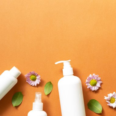 Turuncu arka planda beyaz banyo şişeleri. Düz konum, üst görünüm, kopyalama alanı. Cilt bakımı ve kaplıca kavramı