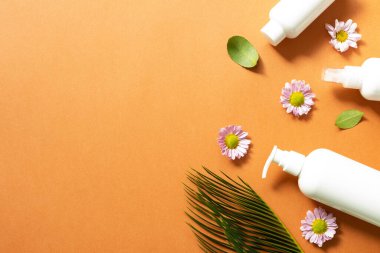 Turuncu arka planda beyaz banyo şişeleri. Düz konum, üst görünüm, kopyalama alanı. Cilt bakımı ve kaplıca kavramı