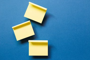 Sarı not defteri mavi arka planda yapışkan bir not. Üst görünüm, boşluk kopyala