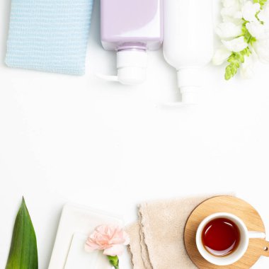 Spa banyo ürünleri. Sabun, duş havlusu, şampuan şişesi, beyaz arka planda çiçekli çay. Üst görünüm, boşluk kopyala