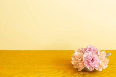 Ahşap masada karanfil çiçekleri vazosu. sarı arkaplan