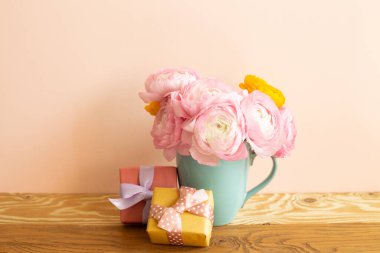 Pembe ranunculus çiçeği buketi ve tahta masada hediye kutuları. pembe arkaplan