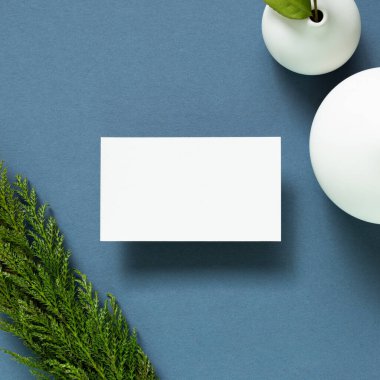 Masasında vazo dolusu bitki olan boş bir beyaz kartvizit. Lacivert arka plan. düz alan, üst görünüm, kopyala boşluk