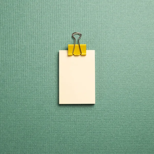 Blank memo pad with yellow metal clip on green background. top view, copy space