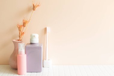 Banyo şişeleri, diş fırçası, beyaz mozaik masa üzerinde bitki vazosu. Pembe duvar arka planı. Cilt bakımı ve kaplıca konsepti. İç mimari