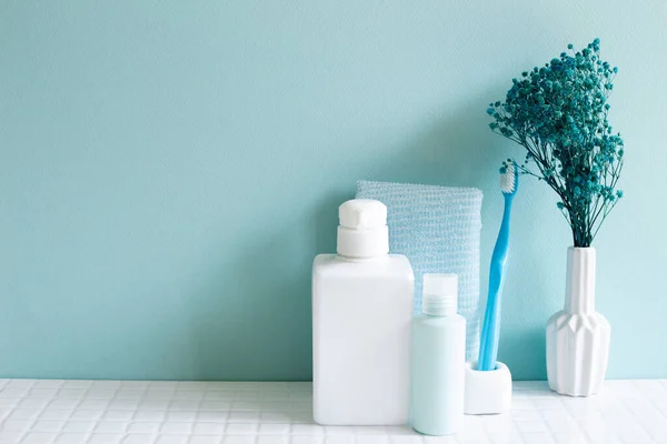 Bathroom bottles, shower towel, toothbrush, vase of plant on white mosaic tile table. blue wall background. Skin care and spa concept. Home interior