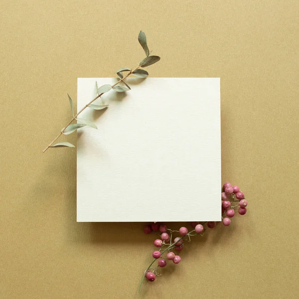 White memo pad with eucalyptus leaf and red fruit on brown background. top view, copy space