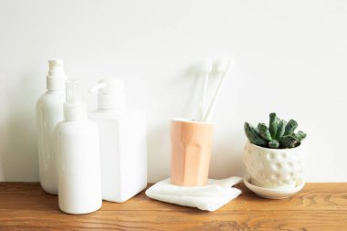 Banyo şişeleri, duş havlusu, diş fırçası, ahşap rafta saksı. Beyaz duvar arka planı. Cilt bakımı ve kaplıca konsepti. İç mimari