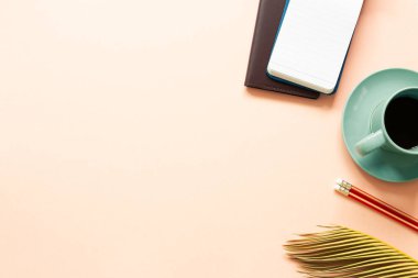 Not defteri, bir fincan kahve, kalem, pembe arka planda yeşil yaprak. Çalışma alanı. Üst görünüm, boşluk kopyala
