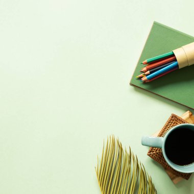 Defter, renkli kalem, kahve, yeşil arka planda yaprak. Çalışma alanı. Üst görünüm, boşluk kopyala