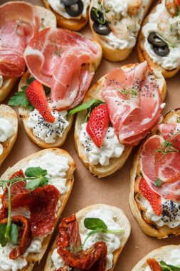 Parti ya da şenlik masası için farklı atıştırmalıklar. Domatesli Ciabatta sandviçi, jamon, krem peynir, sebze, ocak ve zeytin. Lezzetli şarap atıştırmalıkları