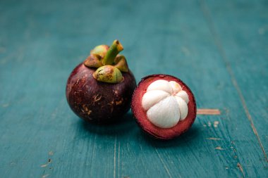 Açık mavi ahşap zemin üzerinde mangosteen meyvesi, tropikal meyve