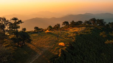 Sarı çadırları olan bir dağ kamp alanının havadan görünüşü. Altın güneş ışığıyla aydınlatılıyor..
