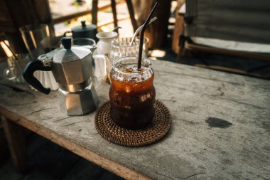 Buzlu, sade kahveyi bir bardakta, kırsal ahşap bir masada moka demliği ile tazeliyorum..