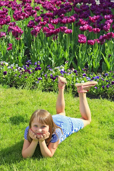 Menina encontra-se na grama perto das tulipas — Fotografia de Stock