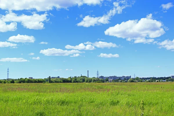 Paisagem de verão com campo de grama e objetos industriais longe — Fotografia de Stock