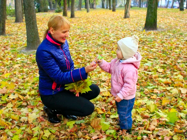 Женщина дарит дочке сладкое в осеннем парке — стоковое фото