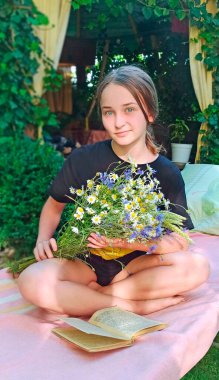 Elinde papatya buketi olan kız kitap okumayı sever. Modern kız dinlenme kitabı okuyor. Bahçede çiçek okuyan kız. Elinde papatya buketi olan genç bir kız kitap ile dışarıda dinleniyor.