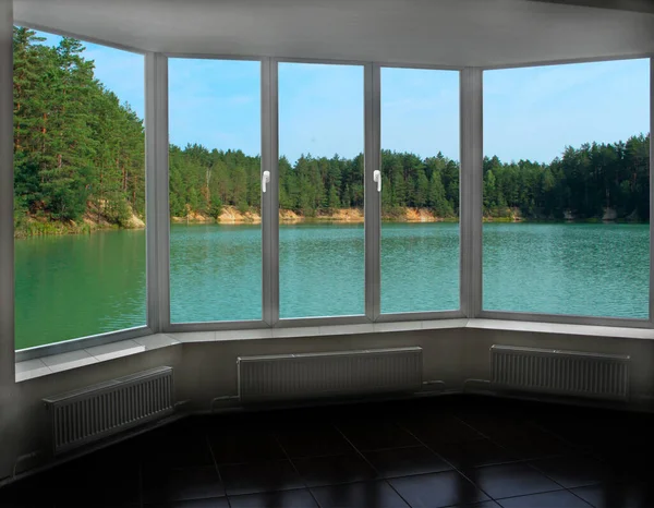 Room with big window with panoramic view to forest lake. Landscape with lake in forest. Panoramic view to nature from room window. View from window