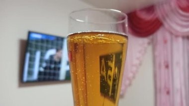 Televizyonun arka planında futbolla birlikte bir bardak bira. Futbol içeceği. Futbol maçı ve bira. Bira bardağında hava kabarcıkları. Televizyondaki yarışma. Futbol maçı izliyordum. Futbol yayını