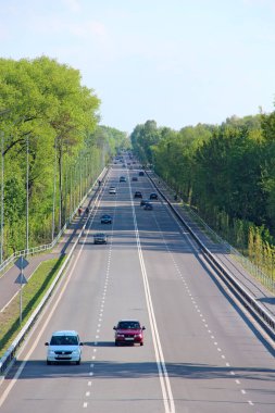 Chernihiv-Ukrayna. 17 Mayıs 2020: Yol kenarlarında yeşil ağaçlar ve arabalar olan otoban panoraması. Yüksek hızlı yol. Otoyolda giden arabalar. Şeritleri ve çalılıkları ayıran asfalt yol