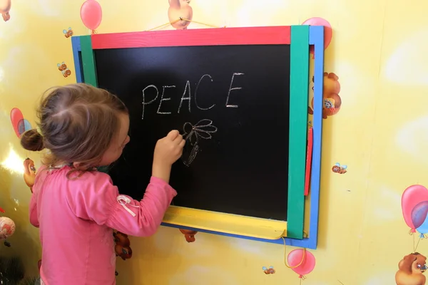 Girl writes on a blackboard a word the peace — Stock Photo, Image