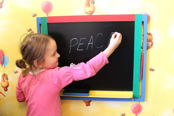 Girl writes on blackboard word the peace — Stock Photo, Image