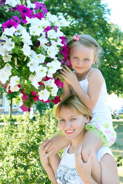 Дочь сидит на своей матери и много цветов в городском парке — стоковое фото