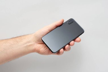 Elinde siyah akıllı telefon tutan adam gri arka planda izole edilmiş.