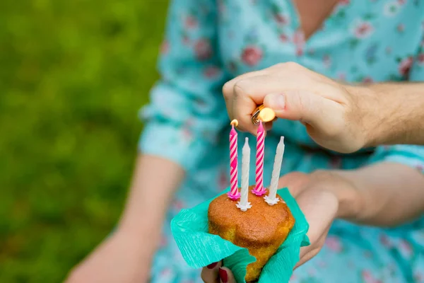 Hand med en tändare för att tända ljuset blåbär muffins på grön bakgrund. bränna fyra ljus på födelsedagen cupcake.Anniversary firande. — Stockfoto