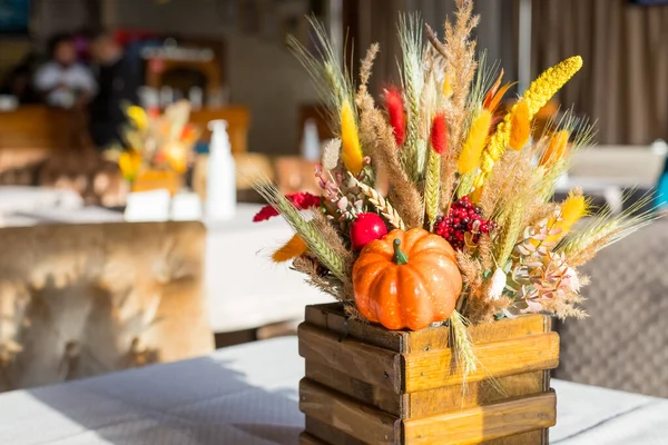 Bouquet of wild flowers in the restaurant. autumn composition in a wooden vase. Autumn interior decor.Orange pumpkin with red berries, dry autumn flowers and yellow leaves .harvest, cozy,festive mood. — Stock Photo, Image