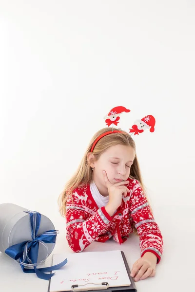 Niña reflexiva escribe carta a Santa Claus sobre fondo blanco.Metas planes sueños hacen que hacer lista para el concepto de Navidad de año nuevo. Órdenes especiales para Santa. chica acostada cerca de los regalos —  Fotos de Stock