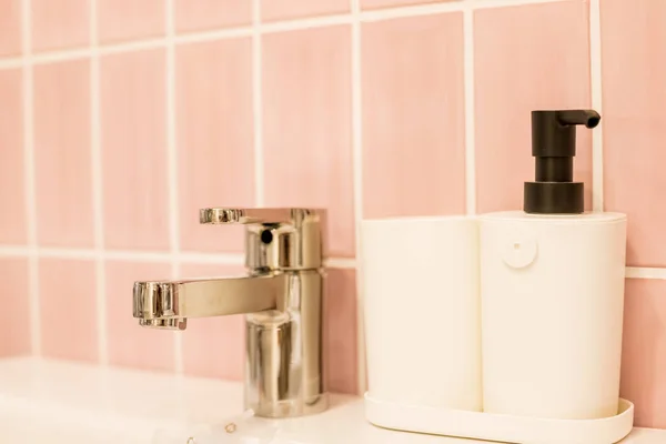 Mermer tezgahlı krom su musluğu, beyaz lavabo. Banyoda lüks musluk karıştırıcısı. Küvet ve su musluğu. Gümüş musluğun yanındaki şişe makinesinde sabun. Hijyenik önleme kavramı. Seçici odak — Stok fotoğraf