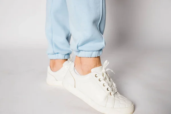 Unrecognizable woman in leather shoes with shoelaces. Womens sports pants. Casual comfortable clothing for everyday.Womans legs in blue pants and white shoes.