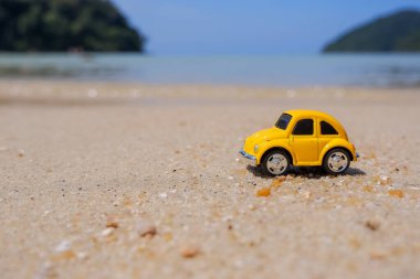 Denize yolculuk, sahilde küçük sarı bir araba. Tatil ve turizm kavramı. Deniz kenarındaki çocuk oyuncaklarına karşı kumlu kumda küçük araba yolculukları içeren kartpostal. Boşluğu kopyala.