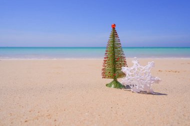Parlak ve güneşli bir günde, okyanus kenarında Noel süsleri, takılar ve noel ağacı. Yeni yıl kavramı. Kumda kar tanesi. Tropik bölgelerde kış tatili, okyanuslarla kumlu plajlar.