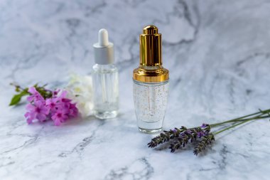 Sıvı kolajen ya da cam şişeli hyaluronik asit mermer zemin üzerinde kozmetik sıvı jel ürünleri ve çiçekler. Güzel cilt bakımı konsepti. Yaş Karşıtı Kozmetik. Seçici odak.