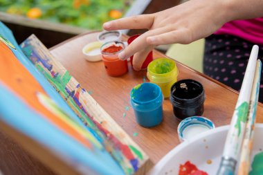 Çocuk resim malzemeleriyle masayı boyuyor. Küçük çocuğu ve yaratıcılık masasını boyamak. Çocuklar yaratıcılığı etkiler. Evde eğitim konsepti çizimi. Kavanozlar boya, boya fırçaları, paletler..