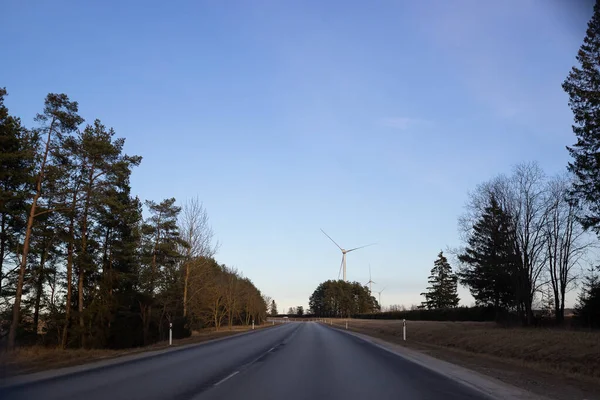 El camino va mucho más allá del bosque y los molinos de viento. Carretera vacía en primer plano, cielo azul con nubes. Fuente de energía alternativa, producción y generación de energía. Ecología y concepto de libertad. — Foto de Stock