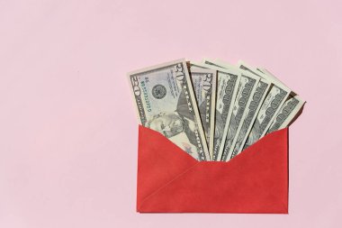 Pembe bir zemin üzerinde kırmızı bir zarfın içinde 100 dolarlık banknotlar. İçinde yazıt tasarrufları ve dolar banknotları olan bir zarf. Mali durumunuzu idare edin ve para biriktirin. Boşluğu kopyala